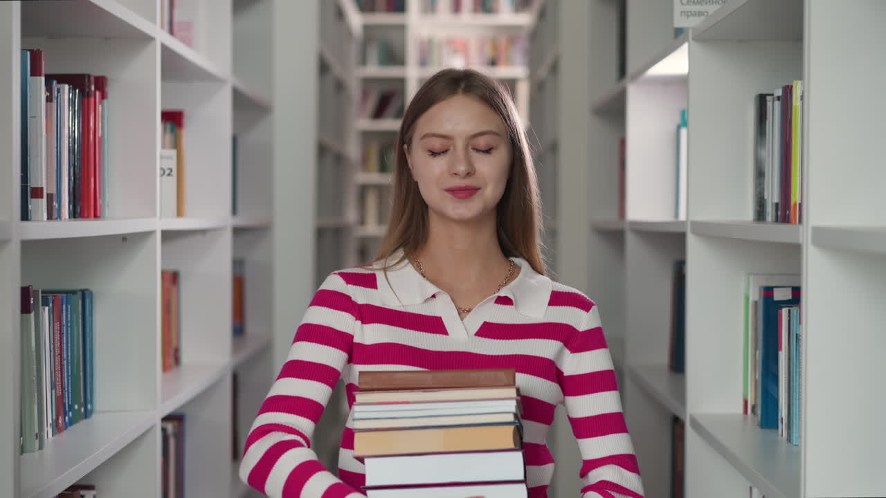 estudiante feliz sostiene libros en el pasillo entre estanterías. mujer rubia lleva literatura para leer en la librería moderna. dama con colección de folio