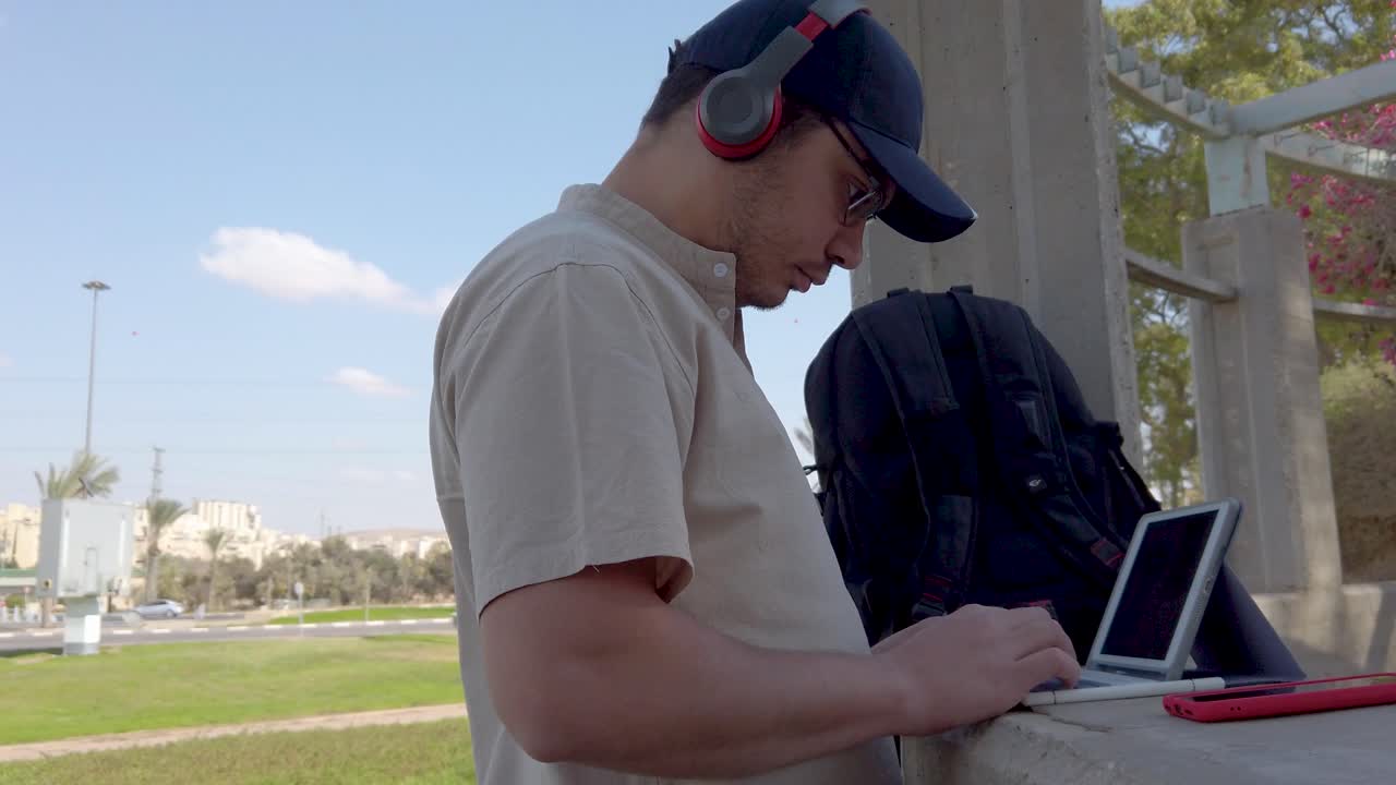 Young man types on a tablet keyboard in a park on a sunny day.