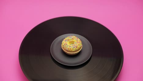 an american donut topped with yellow chocolate with  colorful crumbs turns in a circle on a black turntable. the shot from above