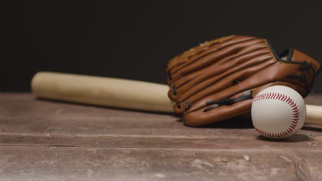 Studio-Baseball-Shot-With-Catchers-Mitt-And-Wooden-Bat-With-Person-Picking-Up-Ball-From-Wooden-Background