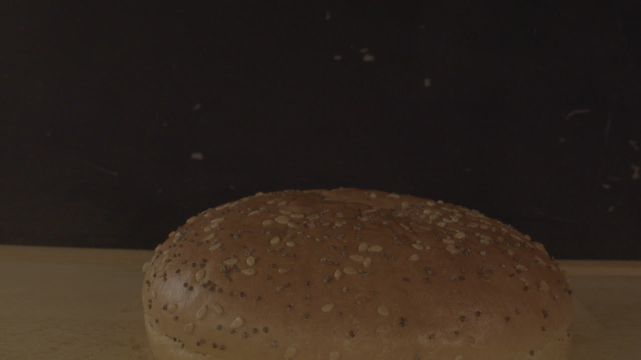 Macro dolly out of hamburger bun on a wooden plate agains a black background