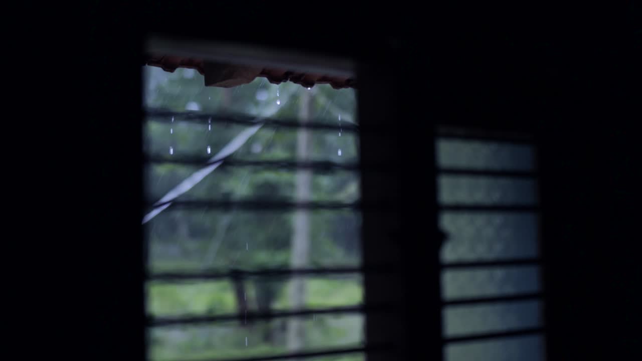 Raindrops dripping from roof during storm, seen from window. Static, shallow focus