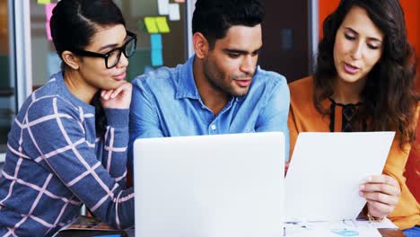 Diseñadores-Gráficos-Sonrientes-Discutiendo-Sobre-Una-Computadora-Portátil-En-Una-Reunión