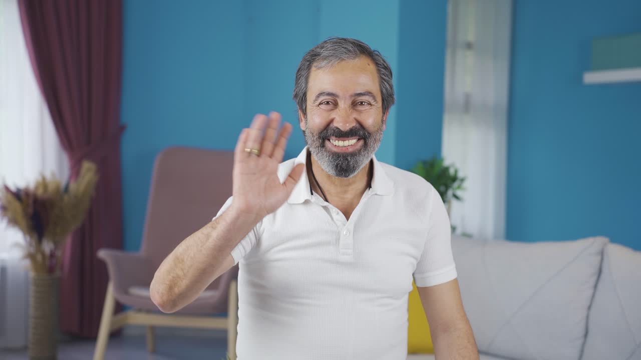 hombre de mediana edad mirando a la cámara y saludando riendo.