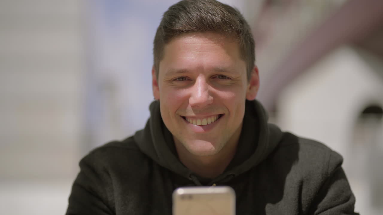 hombre usando teléfono móvil y sonriendo a la cámara