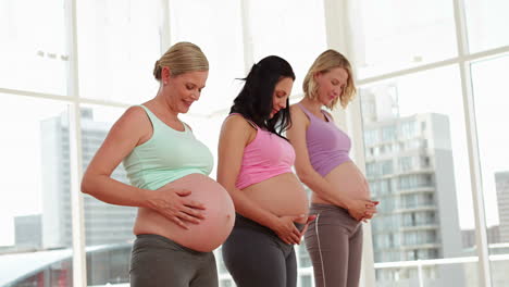 mujeres embarazadas de pie en el estudio de fitness frotando sus protuberancias