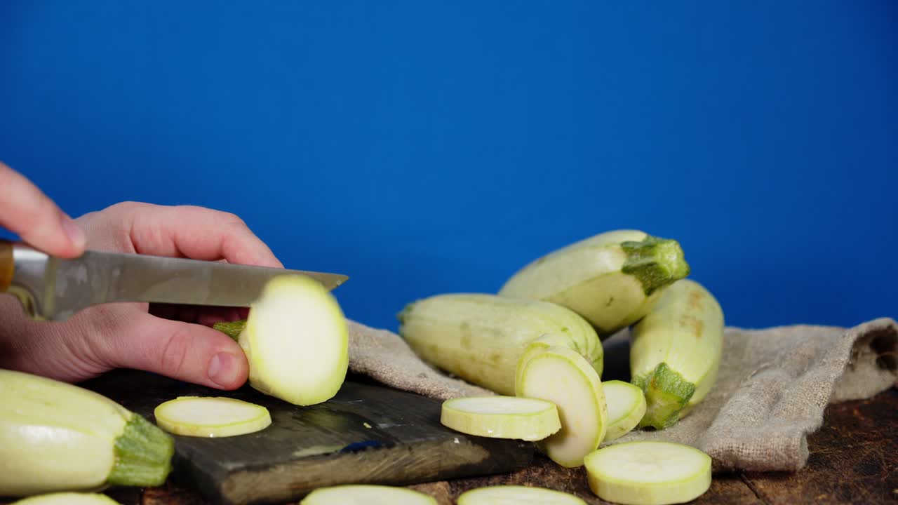 manos masculinas cortando calabacín en una tabla de cortar.