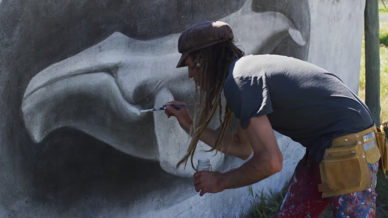 Video of caucasian male artist with dreadlocks painting whale mural on wall