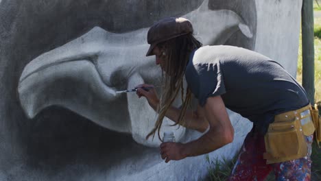 video of caucasian male artist with dreadlocks painting whale mural on wall