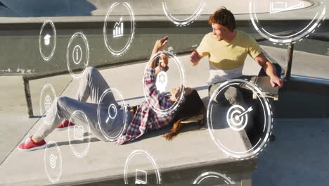 technology icons animation over people relaxing and using smartphone outdoors