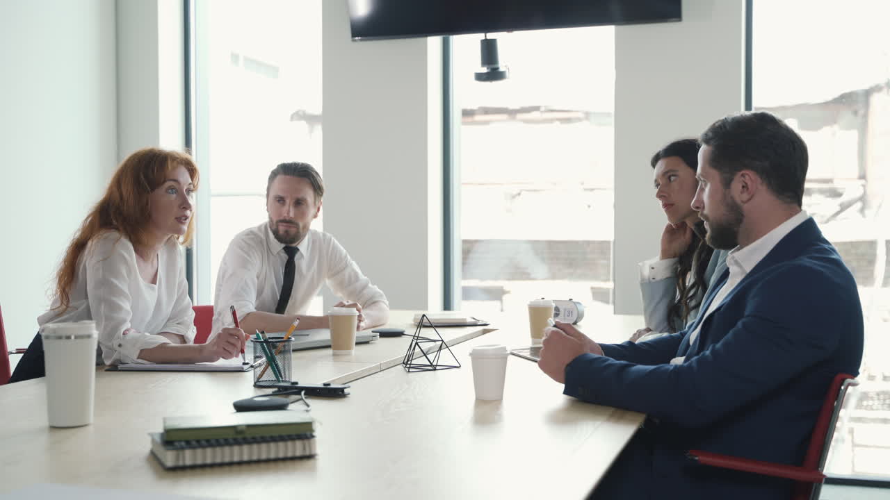 A red-haired businesswoman gives directions to her work team in a business meeting