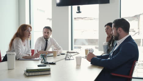 a red-haired businesswoman gives directions to her work team in a business meeting