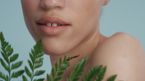 close up portrait beautiful mixed race woman touching body with leaf caressing smooth healthy skin complexion enjoying playful natural beauty on blue background skincare concept