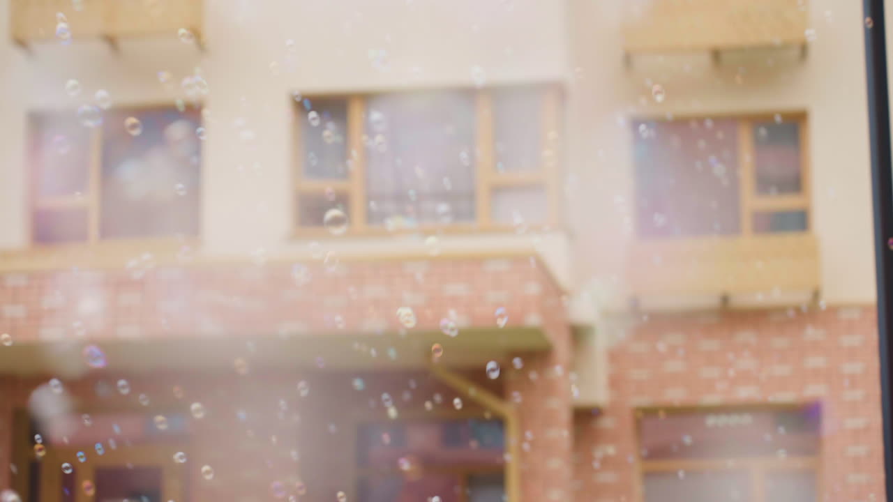 Close up of soap bubbles drifting through air before tall building facade, soft blur windows and balconies behind, gentle breeze carries shimmering spheres upward, creating light playful atmosphere