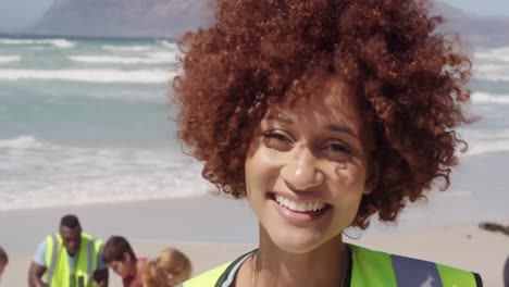 Front-view-of-African-american-female-volunteer-looking-at-camera-on-the-beach-4k