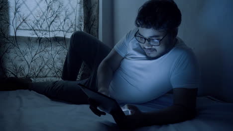 hombre indio con un traje casual usando una tableta digital a última hora de la noche en la cama para charlar