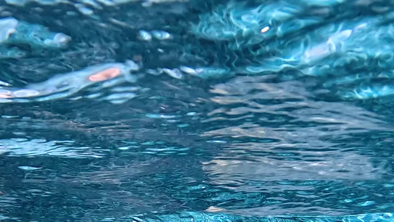 Dettaglio astratto di increspature luccicanti di acqua blu e riflessi di luce in una piscina.