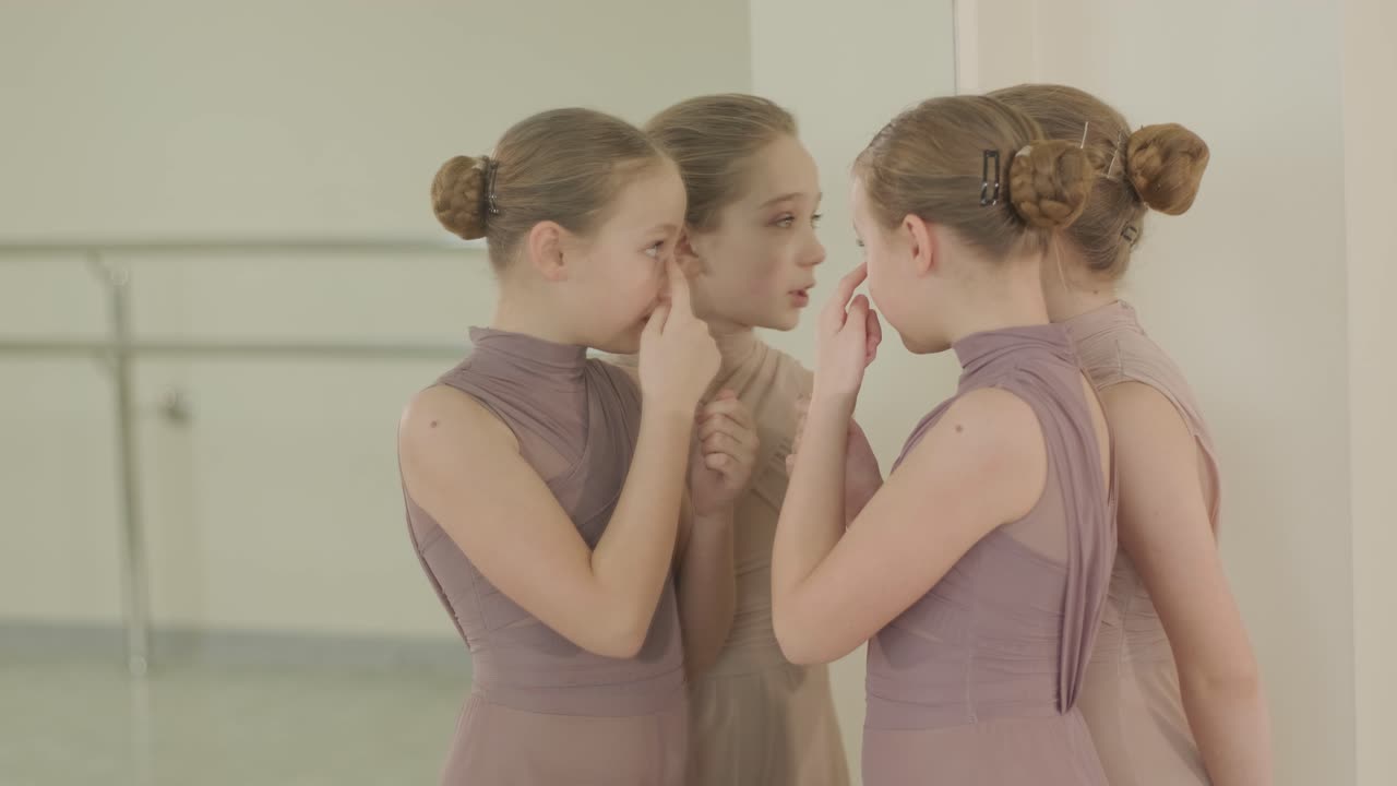 검은색 댄스웨어를 입은 젊은 발레 학생들이 나무 바닥과 벽에 장착된 바를 가진 넓은 발레 스튜디오에서 자세를 연습하는 그룹.