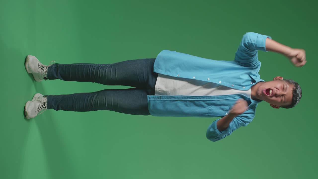 Full Body Of Cheerful Young Asian Boy Celebrating While Standing On Green Screen In The Studio