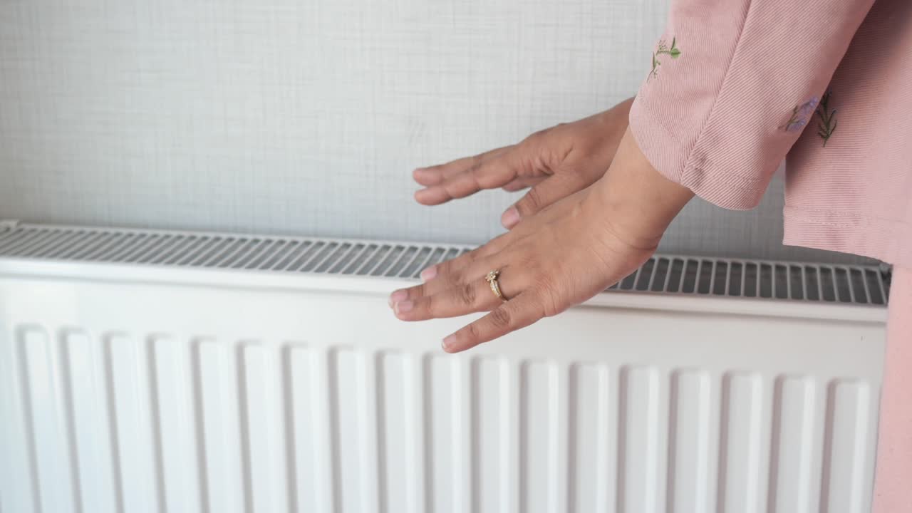 Woman warming hands near electric heater at home