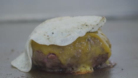 close-up of a cheeseburger on a restaurant grill as a fried egg is placed on top of it