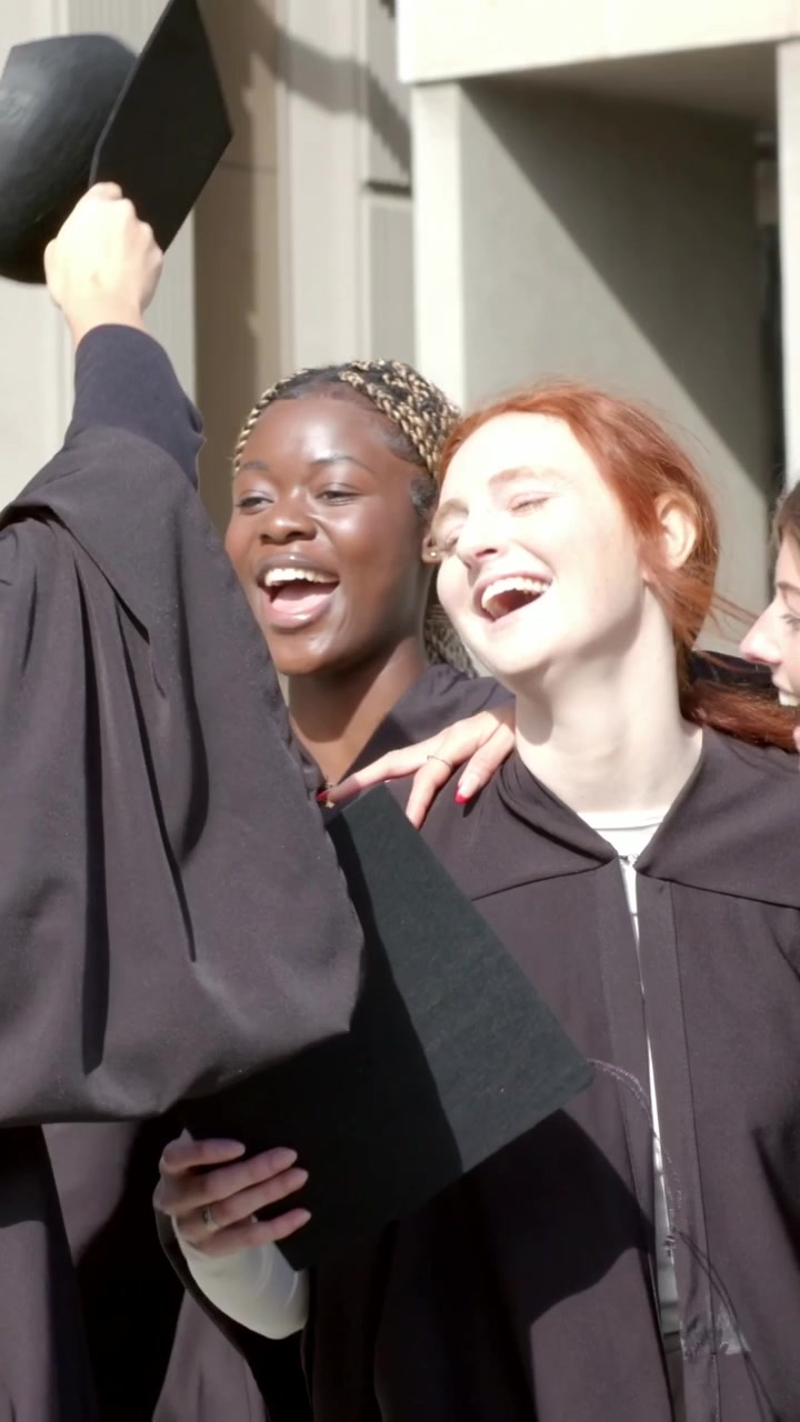 Video verticale: lancio del tocco, tre laureati che esultano per la laurea, sistemano i tocchi nel campus in toga nera.