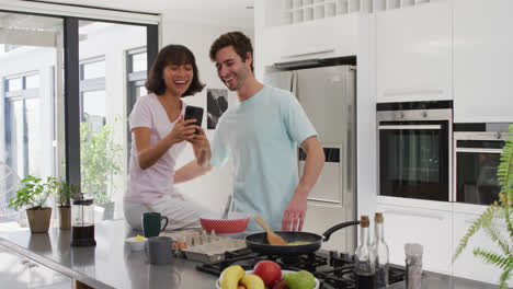 video de una pareja feliz y diversa usando un teléfono inteligente en la cocina