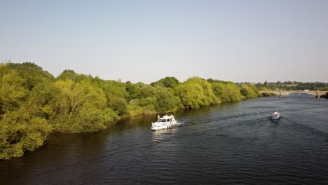 a river boat and narrow boat pass each other in opposite directions on a sunny, summers day on the river trent in the nottinghamshire countryside.