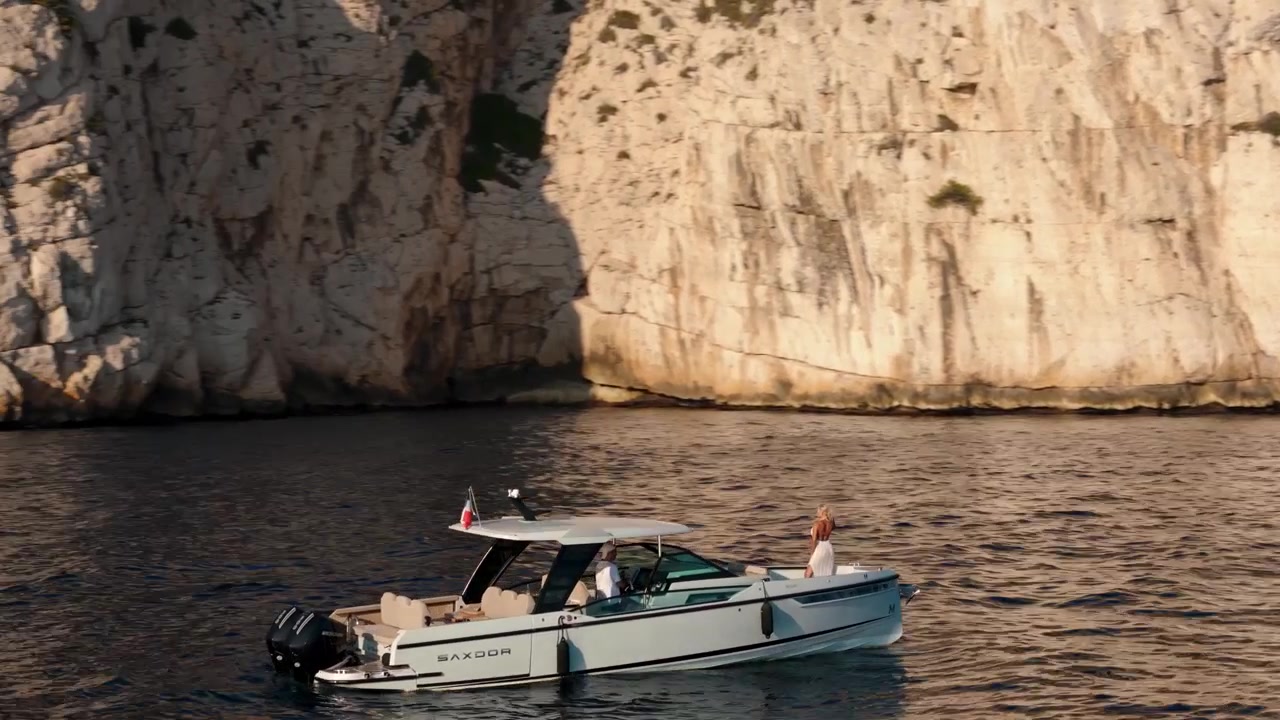 Donna bionda su uno yacht vicino a una scogliera rocciosa a Nizza, Francia