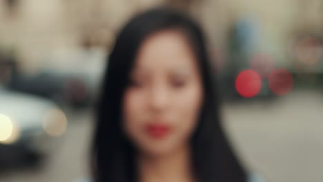 거리에서 야외 카메라를 향해 웃고 있는 젊은 미모의 여성을 닫고 처음에는 흐릿한 다음 초점을 맞춥니다.