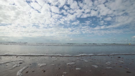 Closeup-of-small-waves-washing-gently-onshore,-high-stratus-clouds-on-the-horizon,-North-Sea,-Belgian-coast