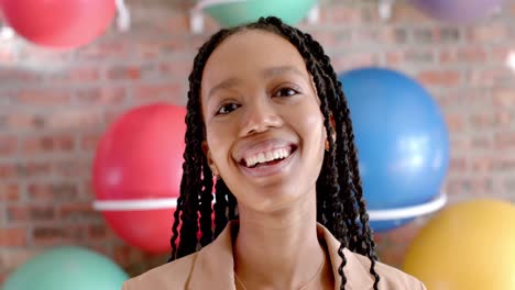 portrait of happy african american casual businesswoman against wall with exercise balls in office