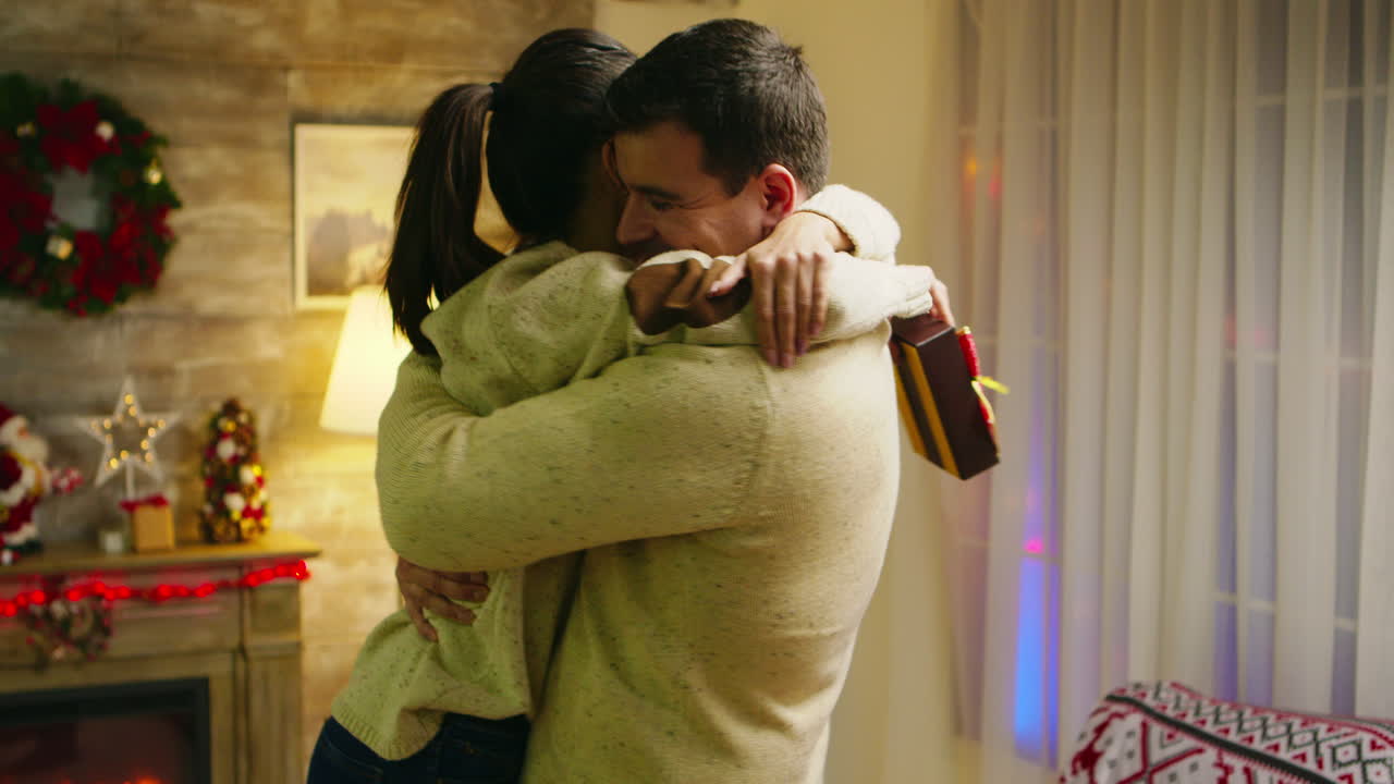 una mujer joven salta en los brazos de su marido sosteniendo un presente.