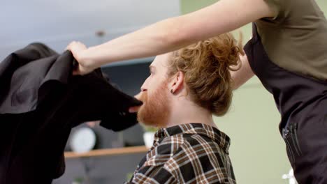 Peluquera-Caucásica-Poniendo-Capa-A-Un-Cliente-Masculino-En-La-Barbería,-En-Cámara-Lenta