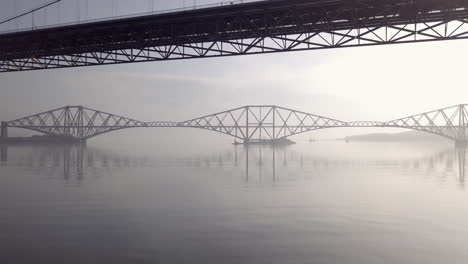 Imágenes-Aéreas-Debajo-Del-Viejo-Puente-De-La-Carretera-Con-El-Puente-Del-Ferrocarril-Al-Fondo-En-Un-Día-Soleado-En-South-Queensferry-En-West-Lothian,-Escocia