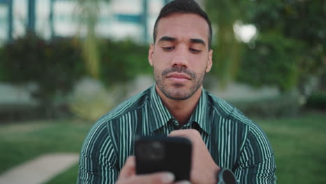 young man checking smartphone sitting in bench outdoors.