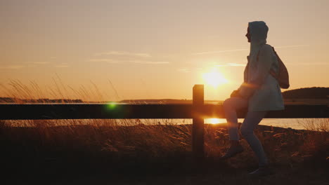 lonely woman silhouette sitting by the fence admiring the sunset over the lake