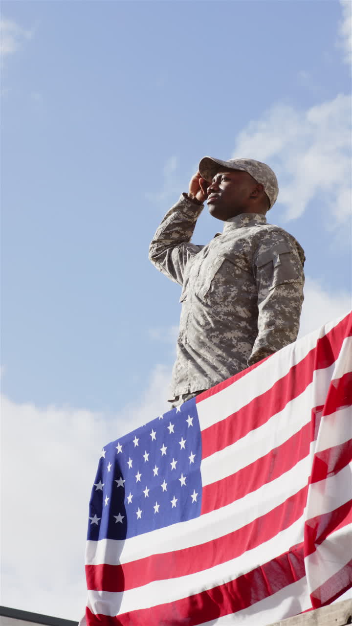 Vertical video: Saluting, soldier in uniform standing by American flag, showing patriotism