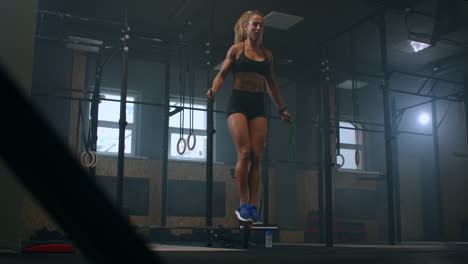 strong muscular young woman rope skipping as warm up. fitness concept. young slim woman jumping with skipping rope in gym. close-up of female feet jumping in mid air whilst using skipping rope.