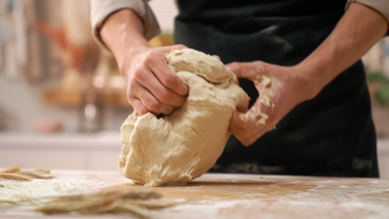 Primo piano delle mani di uno chef che impastano la pasta su un tavolo di legno.