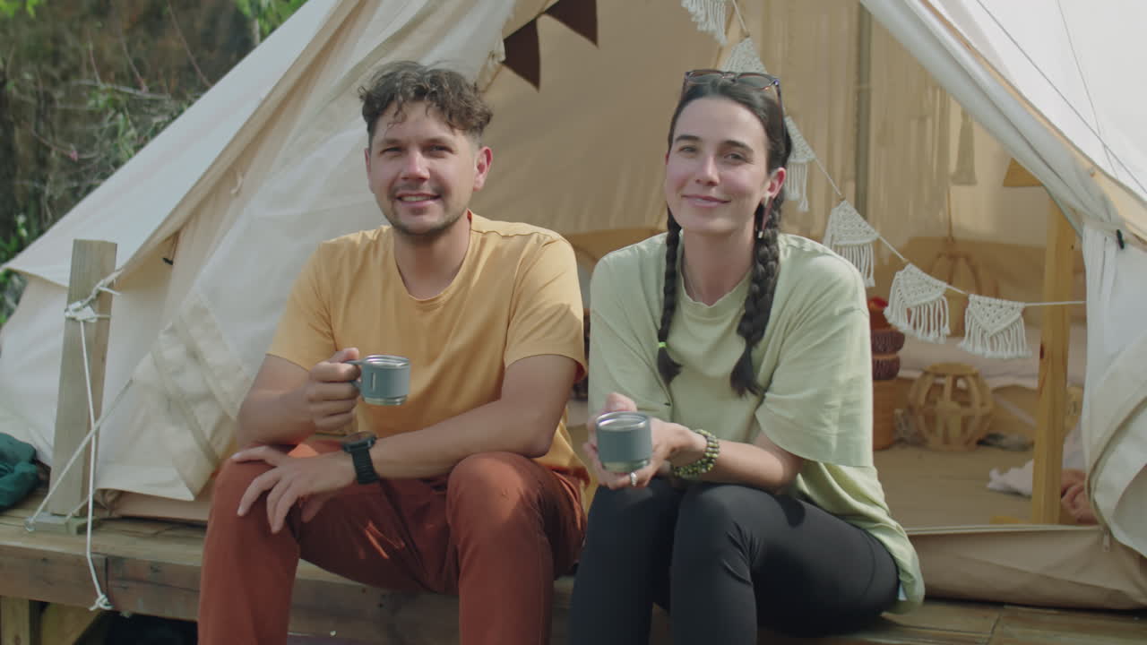Portrait of Cheerful Couple with Tea Mugs by Glamping Tent