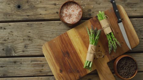 Video-of-two-fresh-asparagus-bundles-on-wooden-chopping-board-with-knife-and-salt-and-pepper