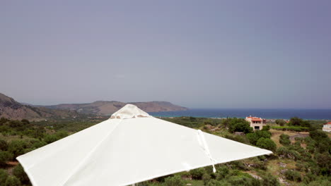 Low-Aerial-Flyover-of-Luxury-Greek-Villa-Patio---Loungers-revealing-Coastline-in-the-Distance-in-Crete,-Greece