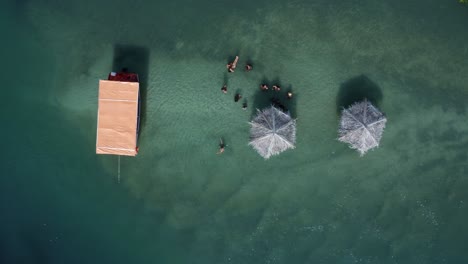 rising aerial drone shot of locals enjoying a small secluded natural turquoise pool with thatch umbrella's branching from the curimataú river near barra de cunhaú in rio grande do norte, brazil