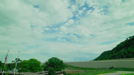 Highway scene featuring American flag, lush roadside greenery, and expansive sky, celebrating truck drivers' patriotism.