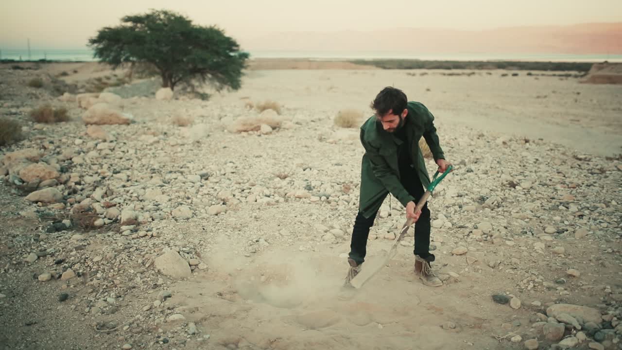 Israeli man use spade to bury items in hole in dry desert soil, shovelling dirt