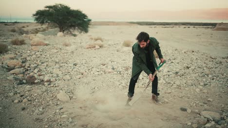 israeli man use spade to bury items in hole in dry desert soil, shovelling dirt