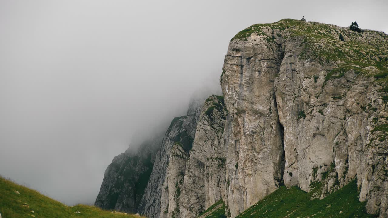 movimiento panorámico de la cámara derecha, que revela un paisaje épico de la cordillera montañosa con niebla y un ambiente de mal humor