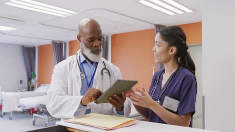 diverse male and female doctors using tablet and talking at hospital
