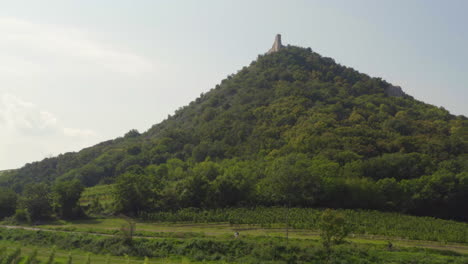 Cyclist-cycling-below-Děvín-hill-with-Děvičky-castle-in-Moravia,-drone